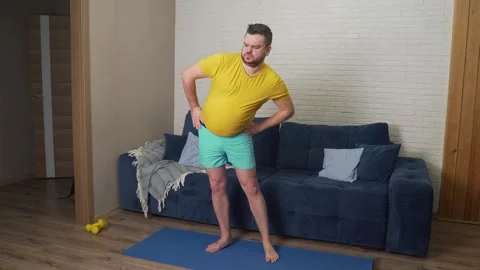 Stout bearded man whimsically and diligently performs hip rotation at home. He Vídeo Stock 169378180