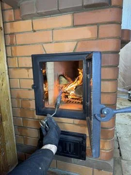 A stove maker lights a test fire in the stove firebox. Firewood and flames ar Stock Photos
