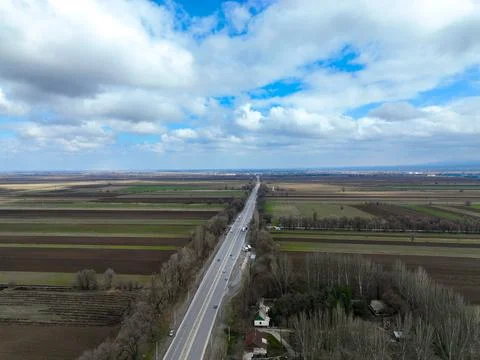 Straight highway bisecting wide patterned fields under a cloudy sky Stock Photos