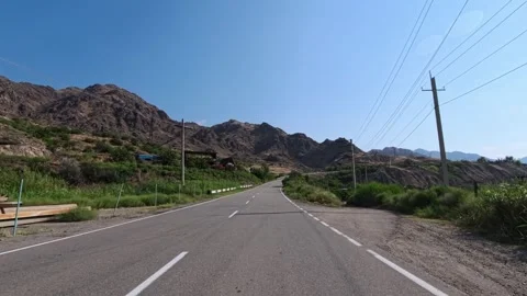Straight road leads through rocky hills with tall green trees on sides Stock Footage 340078643