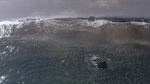 Straight shot of peaceful waves roll into a black sand beach shore paradise Stock Footage 103223526