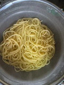 Straining water from boiled spaghetti with help of a strainer in the kitchen Stock Photos