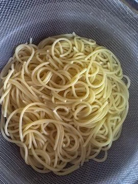 Straining water from boiled spaghetti with help of a strainer in the kitchen Stock Photos