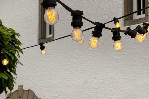 Strand of decorative light bulbs illuminates European courtyard Stock Photos