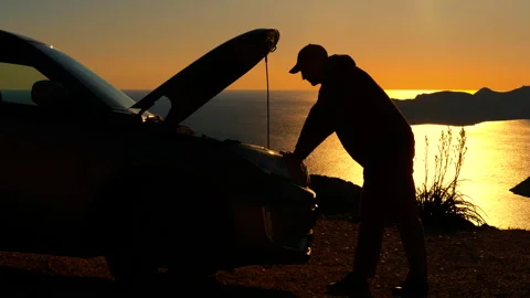 Stranded man inspecting broken car engine at sunset. Stock Footage 332675656