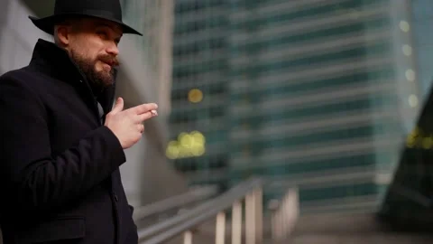 Strange man in black coat and hat is smoking cigarette and waiting someone on Stock-Footage 165939310