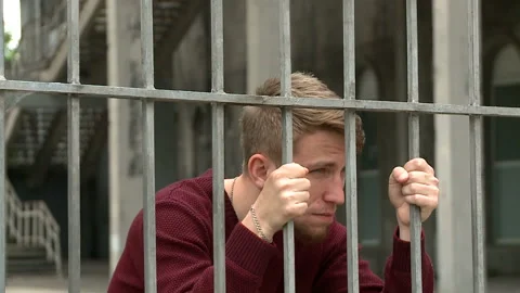 A strange young man is looking through the bars, a fence Stock Footage 134249750