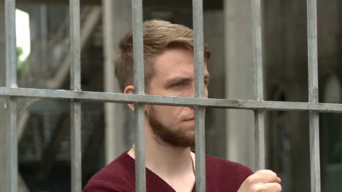 A strange young man is looking through the bars, a fence Stock Footage 134250601