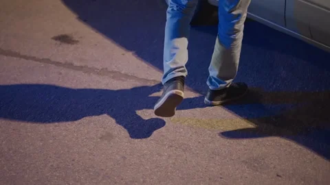 Stranger moving stealthily across cracked pavement toward parked silver car Stock Footage 329448495