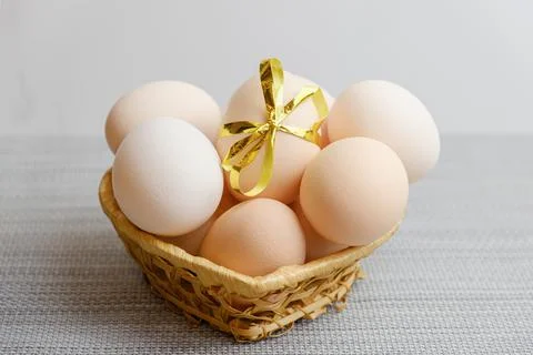 Straw basket with chicken eggs lying in it. One of the eggs is tied with a fe Stock Photos