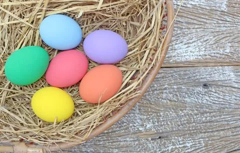 Straw basket with easter eggs on wooden background Stock Photos