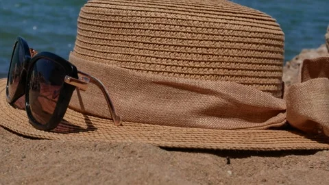 Straw beach hat, black sunglasses on sandy beach against blue sea background. Stock Footage 311974516