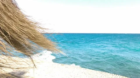 Straw beach umbrella and turquoise ocean waves. Peaceful view from under a straw Stock Footage 334215976