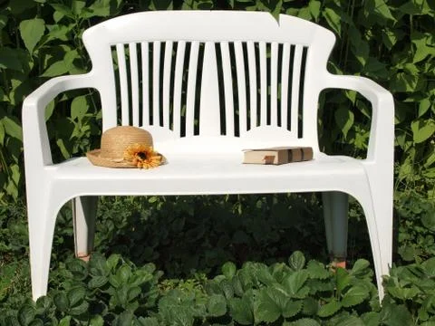 Straw hat and the book on a white bench. Stock Photos
