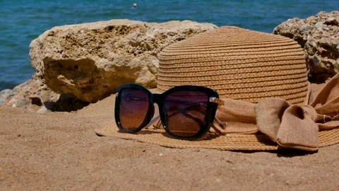 A straw hat and sunglasses on the sandy beach next to the rocks. In the Stock Footage 279536735