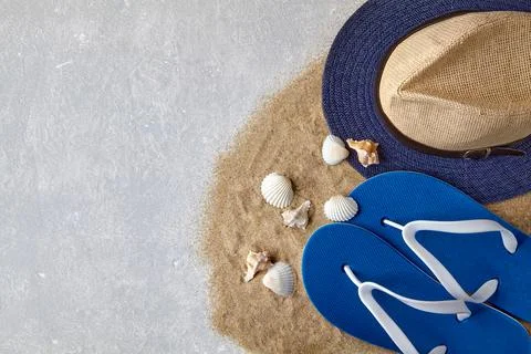 Straw hat, flip flops and seashells on scattered sea sand Stock Photos