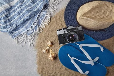 Straw hat, flip flops, seashells, camera and neckerchief on scattered sea san Stock Photos