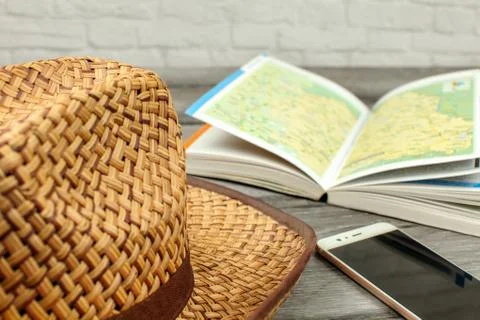 Straw hat, guide book with map, and mobile phone on gray wood desk. Travel pl Stock Photos