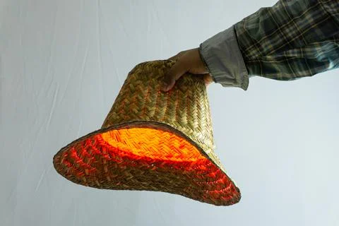 Straw hat held in hand with red light reflecting off surface, traditional a.. Stock Photos