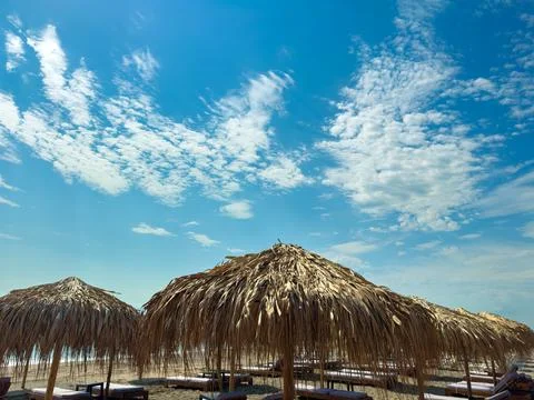 Straw huts stand on sandy ground with a clear blue sky above and clouds scatt Stock Photos