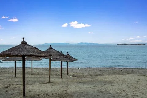 Straw parasol in row on empty sandy beach. Winter day, rippled sea, blue sky  Foto stock
