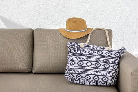Straw sunhat and patterned bag on beige outdoor sofa in bright summer setting Stock Photos