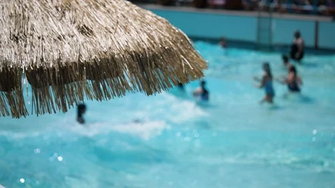Straw umbrella blowing while kids in the background playing and swimming 動画素材 92380441