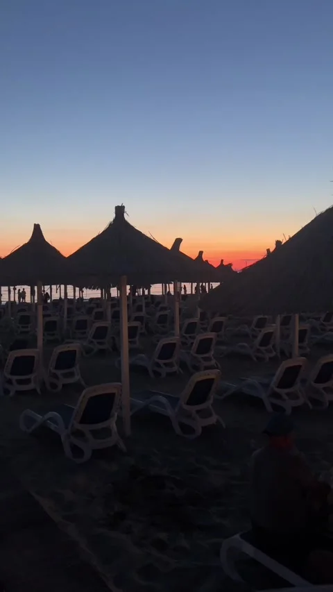 Straw Umbrellas and Sunbeds on Beach at Orange Dusk Horizon in Golem, Albania Stockbeeldmateriaal 343392170