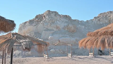 Straw umbrellas on the background of sand and a small mountain Stock Footage 271140991