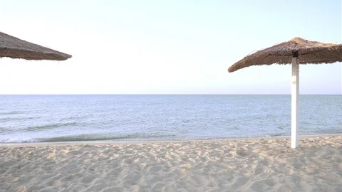 Straw umbrellas on an empty beach early in the morning. Waves of the blue sea. Stock Footage 110999810