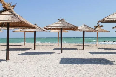 Straw umbrellas at empty beach on summer day Stock Photos