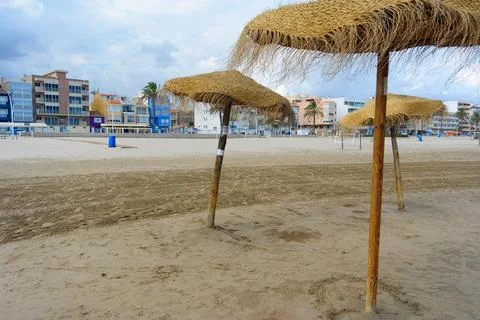 Straw umbrellas stand on empty beach near resort buildings Stock Photos