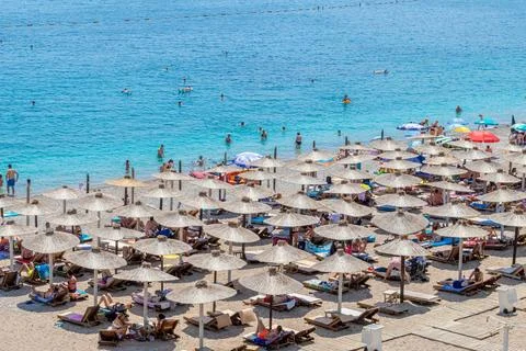 Straw umbrellas stand in rows on a crowded shore, close-up Stock Photos
