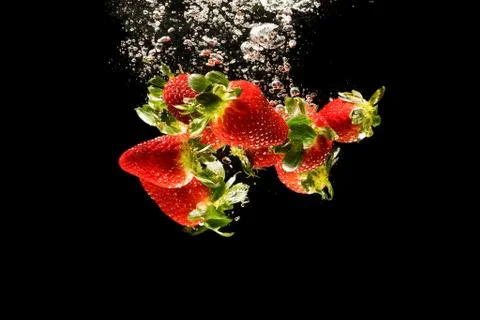 Strawberries falling into water causing bubbles all around it. Healthy food c Stock Photos
