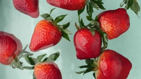 Strawberries gently float in crystal-clear water, their vibrant red hue Vidéo 270320476