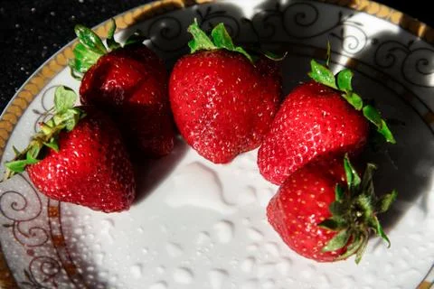 Strawberries on a white plate with a gold pattern. Ripe summer berries in dro Foto stock