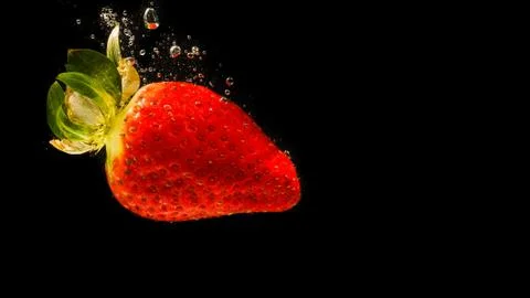 Strawberry falling into water causing bubbles all around it. Healthy food con Stock Photos