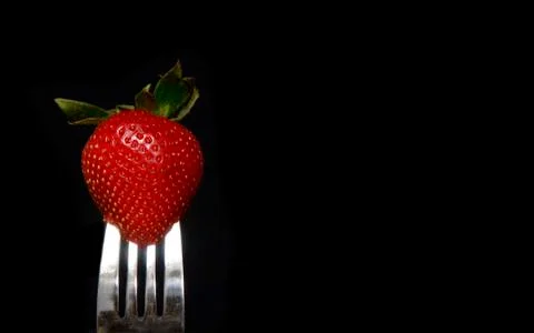 Strawberry on fork on black Stock Photos