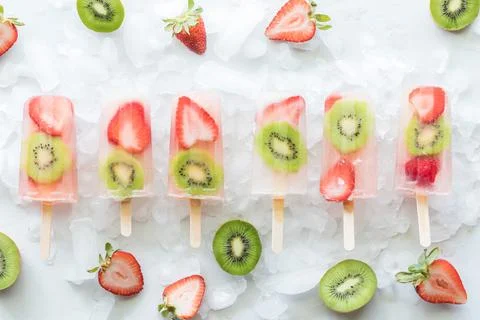 Strawberry kiwi popsicles on ice surrounded by slices of strawberries and kiwi. Stock Photos