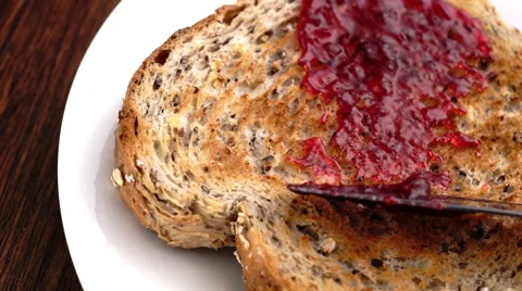 Strawberry raspberry jam being spread on whole wheat multi-grain bread in slow Stock Footage 46880970