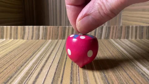Strawberry-shaped top spinning close up on a fabric surface Stock Footage 261785540