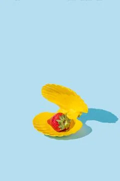 Strawberry in a yellow seashell instead of pearl on a blue background. Stock Photos