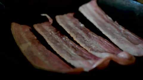 Streaky bacon rashers frying in a cast iron skillet Stock Footage 132504120