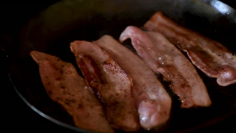 Streaky bacon rashers frying in a cast iron skillet Stock Footage 132504777