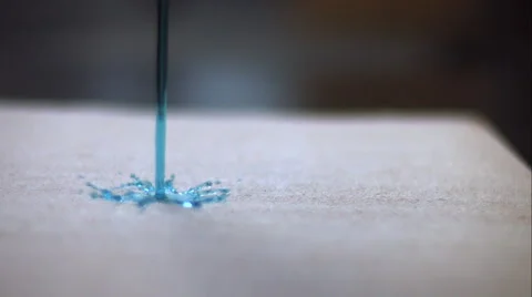 A stream of blue liquid hits the ground and explodes in all directions. Stock Footage 64875809