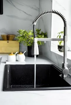 A stream of clean water drink flows from the kitchen faucet into the sink Stock Photos