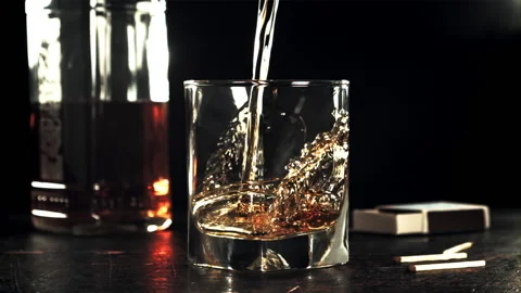 A stream of cognac pours into a glass on the table. Filmed on a high-speed Stock Footage 169476752