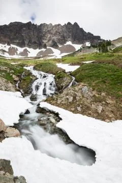 Stream cuts under a snow bridge in high mountain cirque Stock Photos