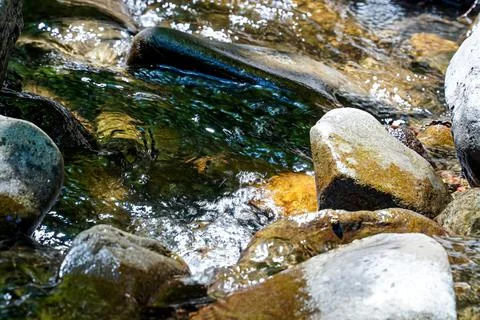 Stream flowing between rocks, sun-heated rock tops sticking out of the water Stock Photos