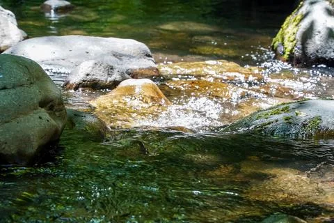 Stream flowing between rocks, sun-heated rock tops sticking out of the water Stock Photos